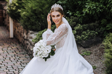 A beautiful bride in a long white dress with a bouquet in her hands, a diadem on her head, sits in...