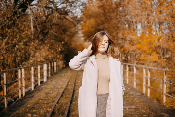 beautiful long-haired woman walks through the autumn streets. Railway, autumn, woman in a coat.