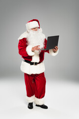 Santa claus in costume using laptop on grey background.