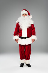 Full length of bearded father christmas looking at camera while standing on grey.