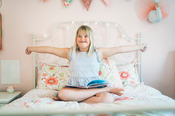 Obraz na płótnie Canvas Beautiful little child girl in a dress having great time on her pink bedroom reading book