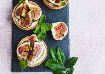 Tartlets pastry with white cream, topped with fig and pistachio on pink background. Cooking concept. Healthy dessert.