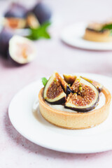 Tartlets pastry with white cream, topped with fig and pistachio on pink background. Cooking concept. Healthy dessert.