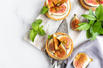 Tartlets with delicate cream cheese and fresh figs decorated with mint and pistachio, grey background. Autumn dessert. National Dessert Day, October 14.