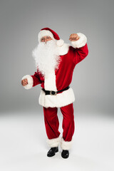 Full length of barded santa claus dancing and looking at camera on grey background.