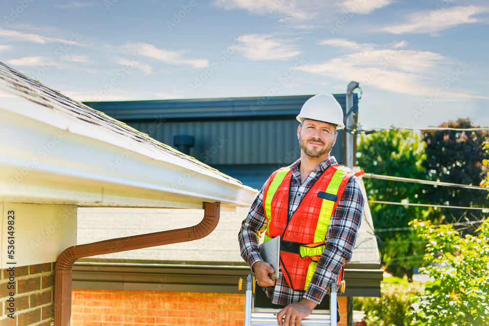 Wall mural man with hard hat standing on steps inspecting house roof