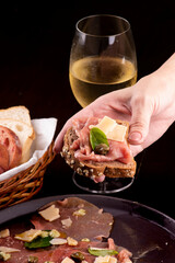 romantic dinner with carpaccio cold meat cattail basket of artisan breads glass of white wine female hand showing a canapé with caper, portrait