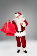 Santa claus pointing at red shopping bags on grey background.
