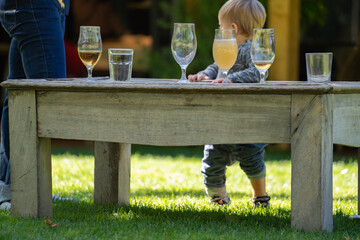 Glasses of beverages on a vintage wooden table against an infant baby and father. Family party in the garden