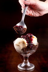 dessert of ice cream cup with brownie and red fruit syrup female hand tasting with spoon close-up...