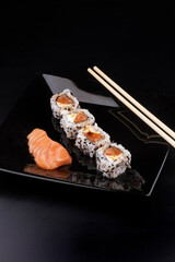 a piece of raw salmon sashimi japanese food on black plate with 4 more salmon and cream cheese sushis with soy sauce and chopsticks in angle view portrait
