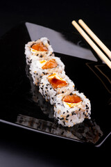 japanese food on black plate with 4 more salmon and cream cheese sushi with soy sauce and chopsticks in close-up angle