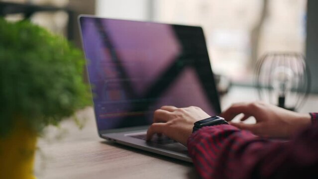 Close up of freelancer's hands typing code on laptop keyboard. Camera slides around developer's figers writing program code on computer display in slow motion. Programmer working on application.