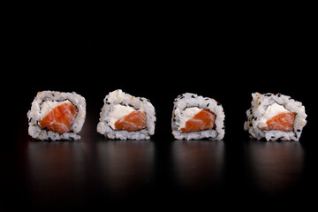 japanese oriental food in with four side by side salmon sushi rolls and cream cheese viewed from the front isolated on black background in closeup