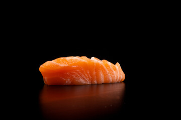 japanese food an isolated piece of salmon sashimi in close up macro photo on black background from standing angle