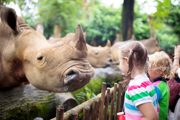 Kids feed rhino in zoo. Family at animal park.