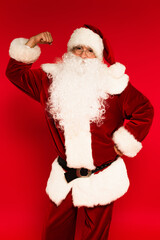 Santa claus in costume showing muscle on arm on red background.