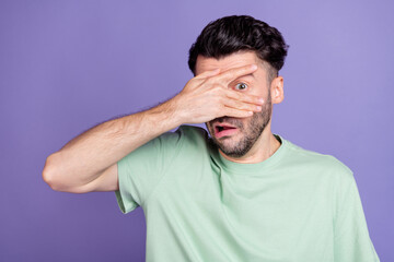 Portrait of scared stressed terrified man with brunet hairdo dressed t-shirt hiding hand cover eye isolated on purple color background