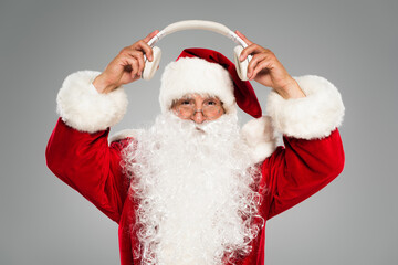 Father christmas in costume holding wireless headphones isolated on grey.