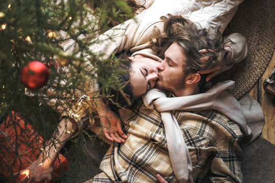 Kissing stylish love couple girl, guy lie on skin on floor in cozy wooden country house,chalet in winter forest.Celebrating new year eve.Gifts,family holiday.Romantic weekend.Decorated Christmas tree