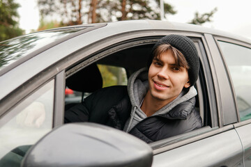 Young smiling man student sitting in his new car. Rent car or buying first car concept.