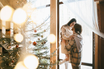 Hugging stylish love couple girl, guy lie on skin on floor in cozy wooden country house,chalet in winter forest.Celebrating new year eve.Gifts,family holiday.Romantic weekend.Decorated Christmas tree