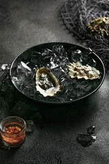 Woman hand hold a fresh opened oysters in a black plate with ice on black textured background.