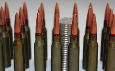 Conceptual image about the price of war. Detailed side view coins column through a group of unitary cartridges lined up on a white background
