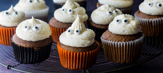 A narrow view of many pumpkin spice cupcakes with ghost icing tops.