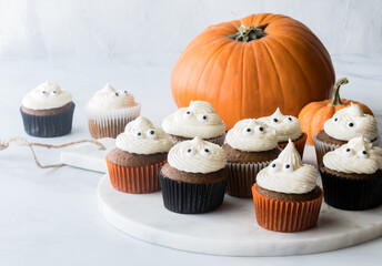 Several pumpkin spice cupcakes on a marble slab with pumpkins in behind.