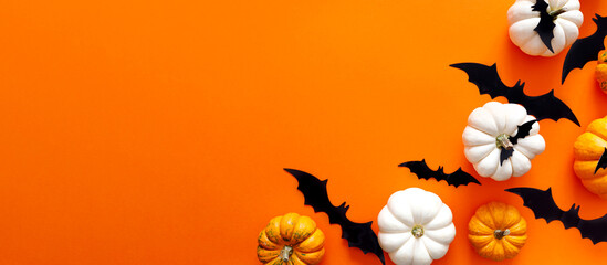 Halloween flat lay composition of black paper bats and pumpkins on orange background. Halloween...