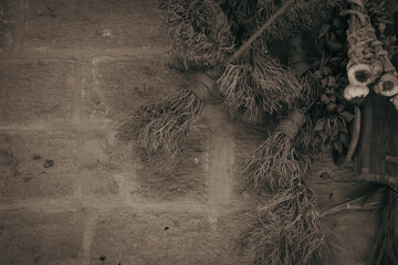 A broom made of shrubs, bunches of garlic, dried flowers and small evil eye beads hung on an old stone wall.