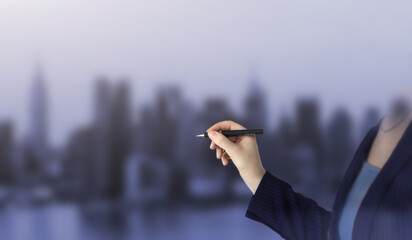 Female hand writing with a pen on city background, black pen in hand. Closeup of hand holding a black marker about to write something.