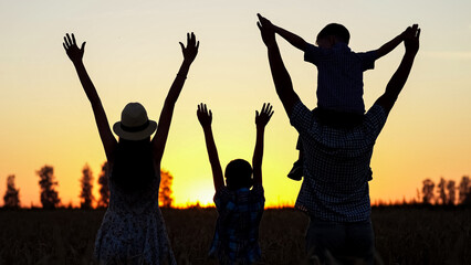 Family members silhouettes raise hands to evening sky. Parents and kids enjoy spending summer holidays together looking at landscape at back sunset