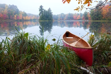 Foto op Canvas Red wood canoe on shore of a small lake with an island on a cloudy autumn morning © Daniel Thornberg