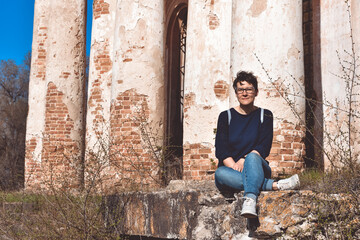 girl with glasses sits against the background of an abandoned building, an abandoned church