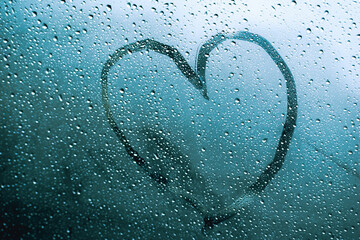 Dibujo de corazón en parabrisas o ventana con gotas de lluvia por fuera, con luz del día nublado...