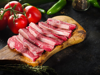 Close-up. Appetizing meat steaks from organic meat from the farm on a wooden cutting board, fresh tomatoes and peppers on a dark background. Recipes for restaurant and home cooking.