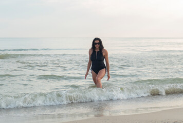 Fototapeta na wymiar Beautiful girl with glasses on the seashore. Brunette in a black swimsuit on the beach.
