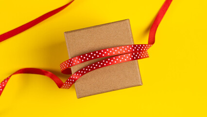 Gift box with red ribbon over yellow paper background