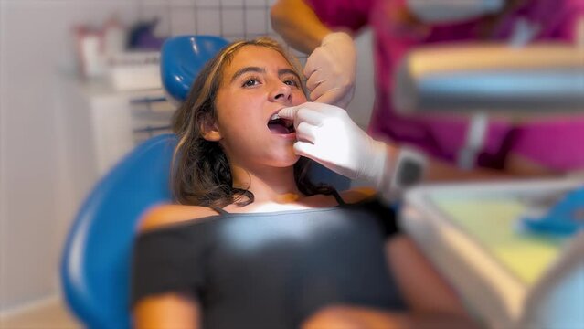 Close up of dentist hand putting elastic rubber band on patient brackets. Girl with wired metal braces on teeth receiving orthodontic treatment