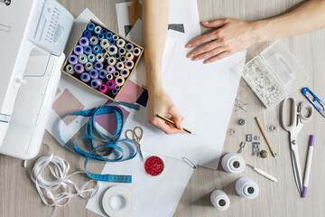 Women's hands draw sketches of dresses with pencil. Top view of sewing items and seamstress tools....