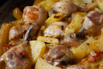 Baked hot potatoes with chicken legs only from the oven. A dish cooked at home. Hot fat and juice heats up, squirts and bubbles on a baking sheet