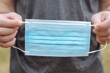 Blue medical mask close-up in male hands due to outbreak of pandemic infection, vaccination,...