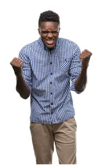 Fototapeta premium Young african american man wearing blue shirt celebrating surprised and amazed for success with arms raised and open eyes. Winner concept.