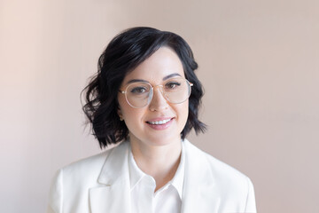 Portrait of a smiling middle-aged brunette in a white jacket and trendy round glasses. Business woman on a plain background of cocoa color.