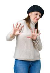 Middle age mature woman wearing winter sweater and beret over isolated background disgusted expression, displeased and fearful doing disgust face because aversion reaction. With hands raised