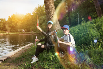 Mom and teen son together on green lawn with soap bubbles in spring public park, having fun in sunny day. Family having rest and fun in good summertime. Concept motherhood, childhood. Copy text space
