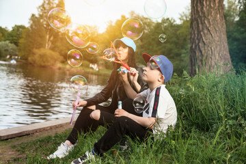 Mother and son having fun on green lawn with soap bubbles in spring public park, together in sunny...