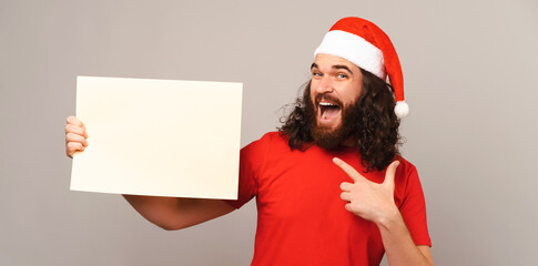 Bearded man holds and points at a white rectangular paper shape at Christmas.